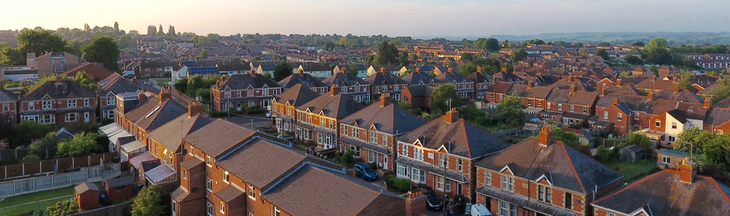 Aerial view of a suburban neighborhood with rows of red-brick houses at sunset. The sky is clear with a warm glow, conveying tranquility.