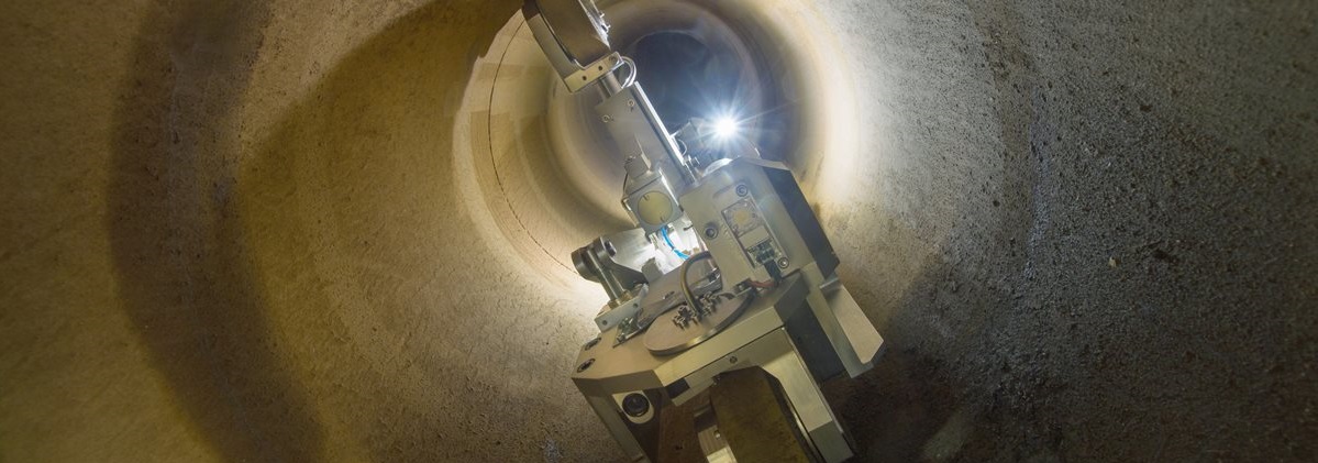 A robotic vehicle with lights navigates inside a large, dimly lit tunnel, examining its interior. The atmosphere is focused and technological.