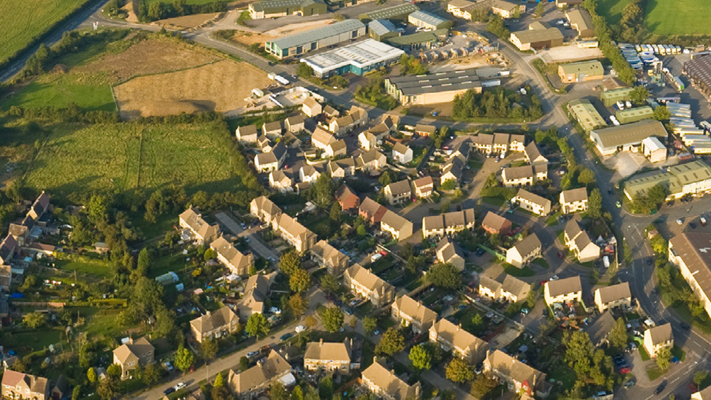 Aerial view showing a residential neighbourhood with rows of houses, roads, green spaces and nearby industrial buildings
