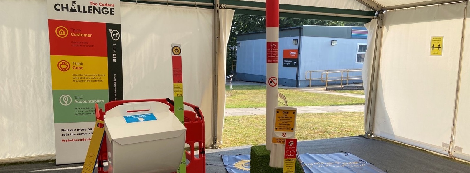 Indoor event tent showcasing safety equipment. Includes a red barricade, a white dispenser, and measurement tools. Informative signs emphasize safety themes.