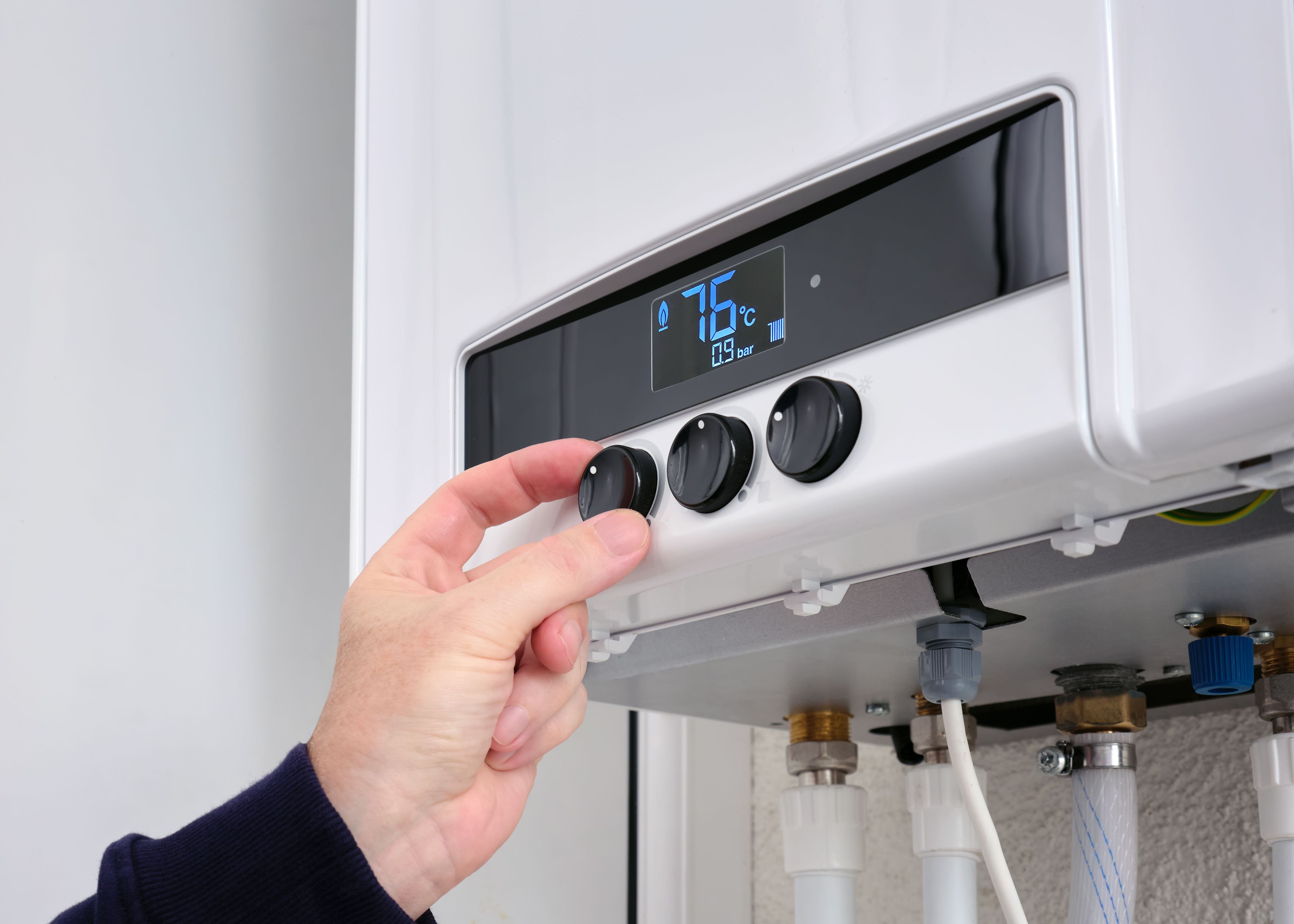 Close up of a man's hand changing the temperature on a modern digital gas boiler. Setting the central heating level on a gas boiler panel.