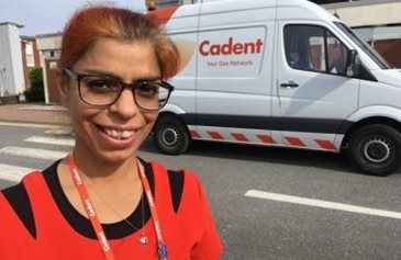 Smiling person with glasses and a red shirt stands on a street in front of a white van labeled 
