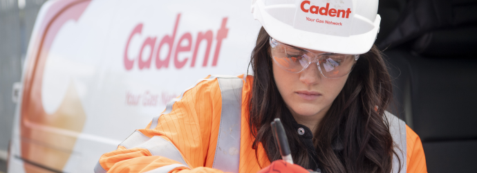 A Cadent engineer in an orange hi-vis safety vest who is writing, with a Cadent van visible in the background.