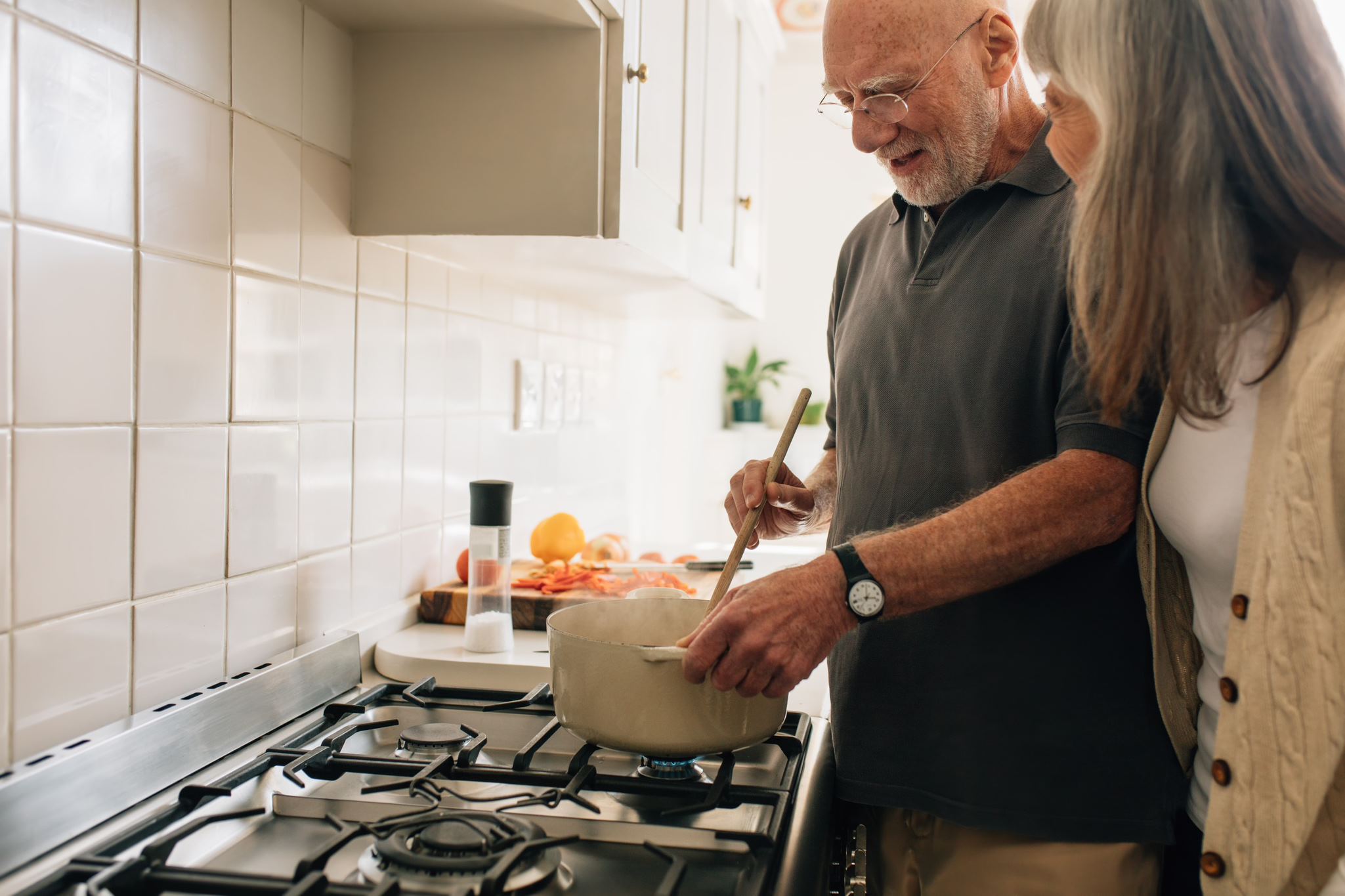 An elder man and woman cooking at a hob