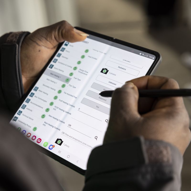 A person holds and interacts with a smartphone in tablet mode using a stylus, navigating through app settings on a screen. The setting is casual and focused.