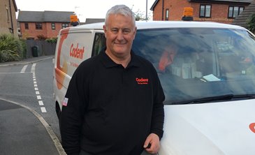 A person wearing a black polo shirt stands smiling in front of a white van with 