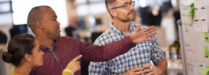 Three individuals in a business setting, two men and one women, planning activity on a large white board.
