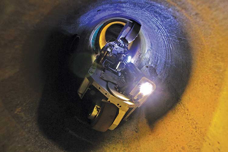 A robotic device with wheels and lights navigates inside a dimly lit, curved tunnel. The blue and orange hues create a high-tech and mysterious atmosphere.