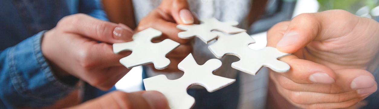 Four hands holding white puzzle pieces