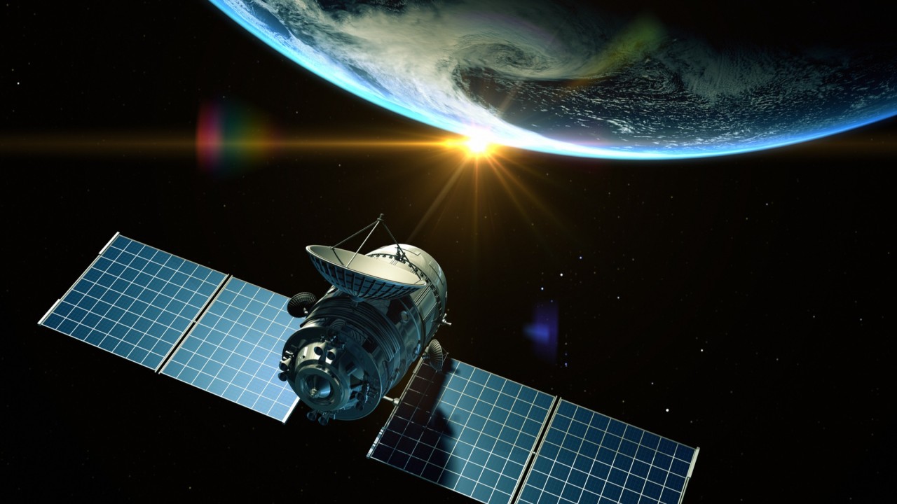 A communication satellite with large solar panels floating in space, with Earth and a bright sunrise visible in the background.