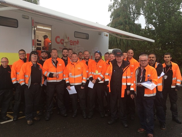A group of smiling people in bright orange safety jackets stands together outdoors in front of a mobile unit, conveying a sense of teamwork and readiness.