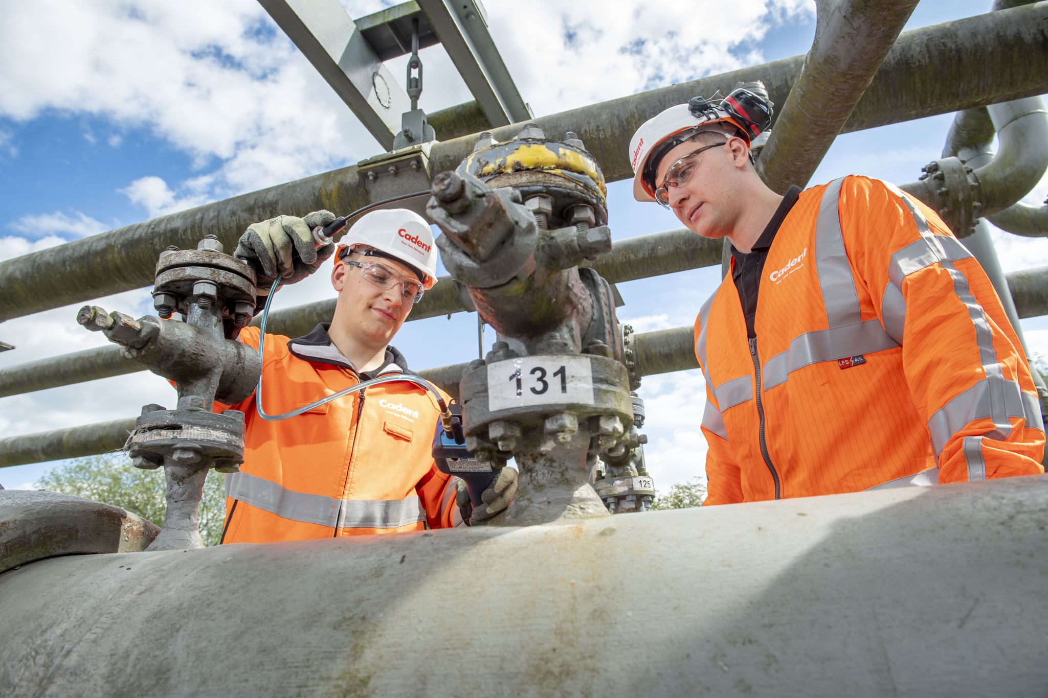Two Cadent engineers stand by a gas pipe whilst one engineer tests the pipe holding a device