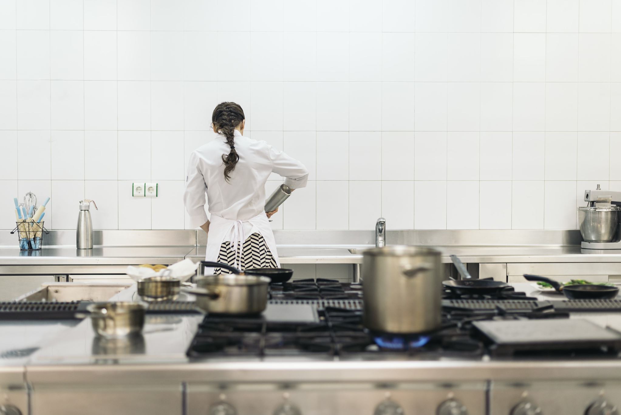 A chef in an industrial kitchen cooking with their back to the camera