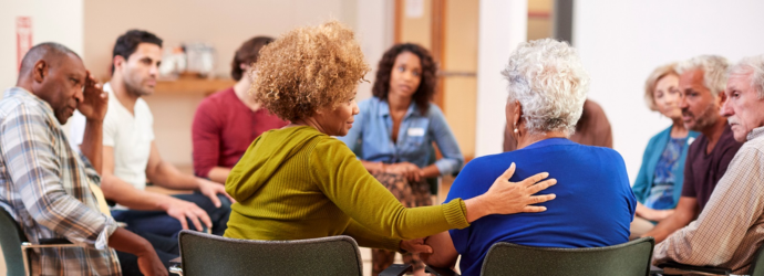 A diverse group of people sits in a circle, engaged in a supportive discussion