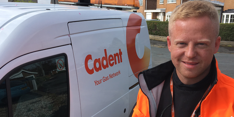 A person in a bright orange jacket stands smiling beside a white van with 
