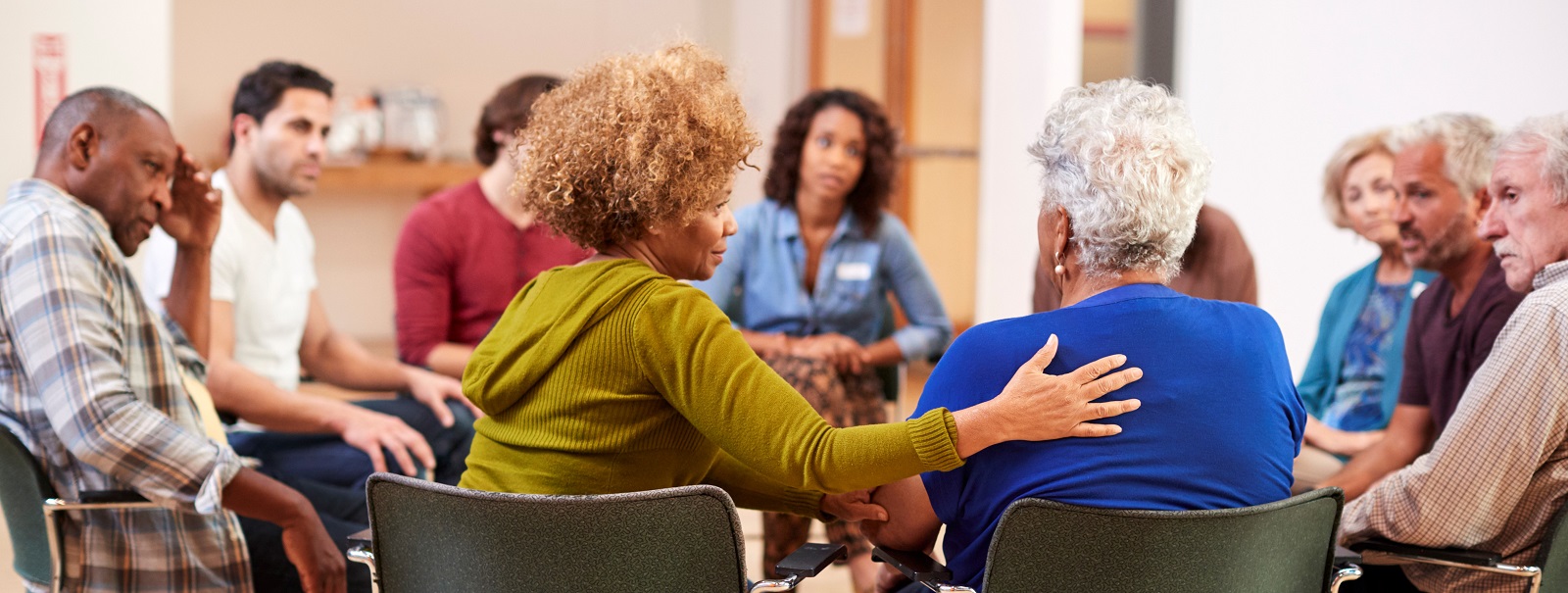 A diverse group of people sits in a circle, engaged in a supportive discussion