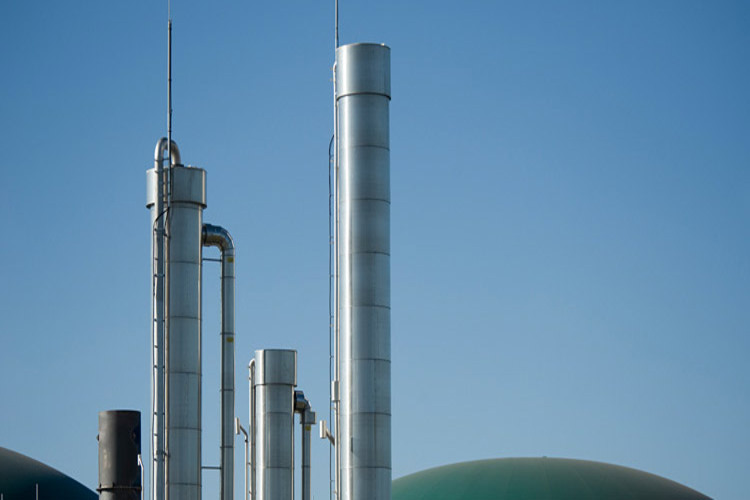 Industrial smokestacks and storage tanks against a clear blue sky