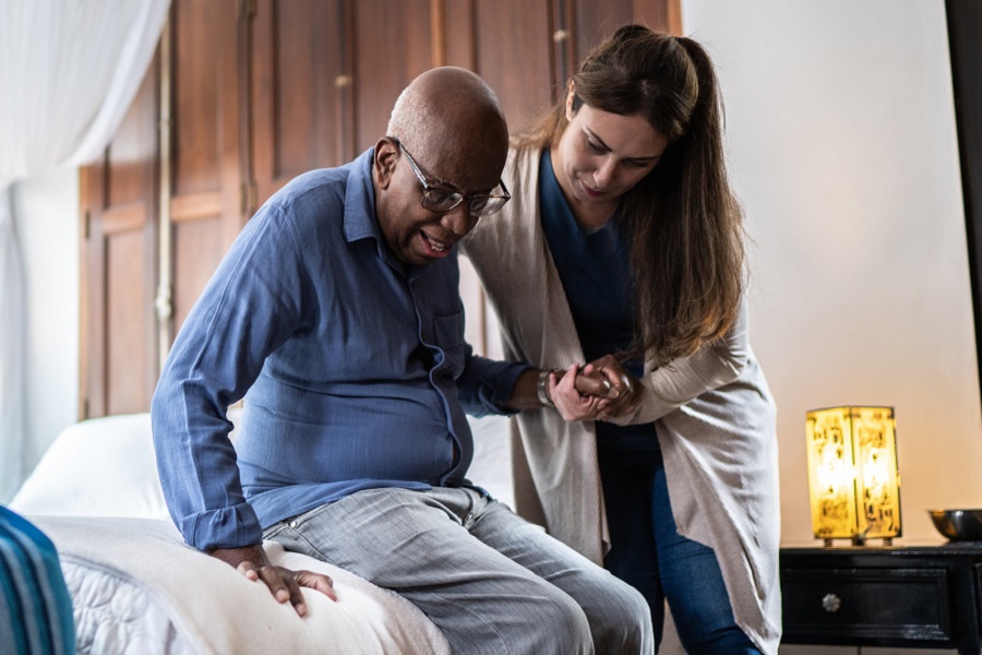 An older gentleman being helped up off his bed by a carer