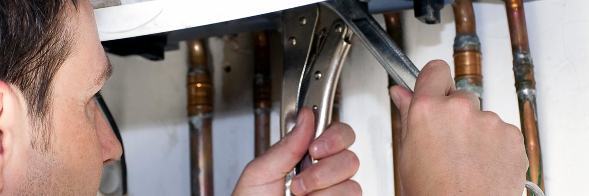 A person uses a pair of pliers to adjust plumbing pipes beneath a sink, surrounded by copper tubing.