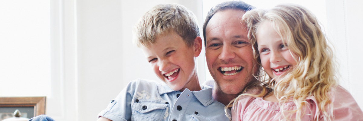A male father figure with two young children, a girl and a boy. In a brightly lit setting