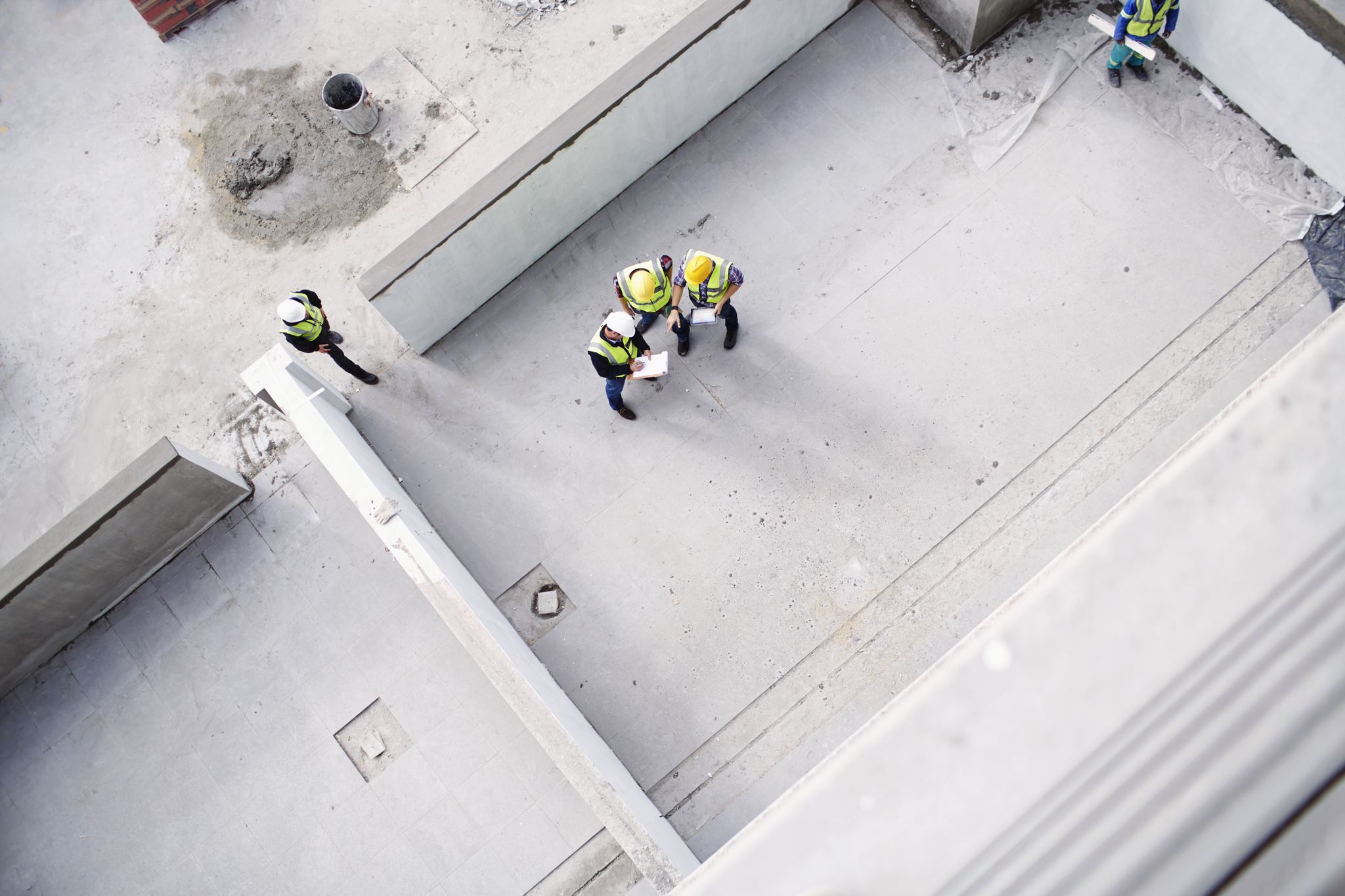 Birdseye view of a construction setting showing a building foundation and workers standing in discussion holding clipboards