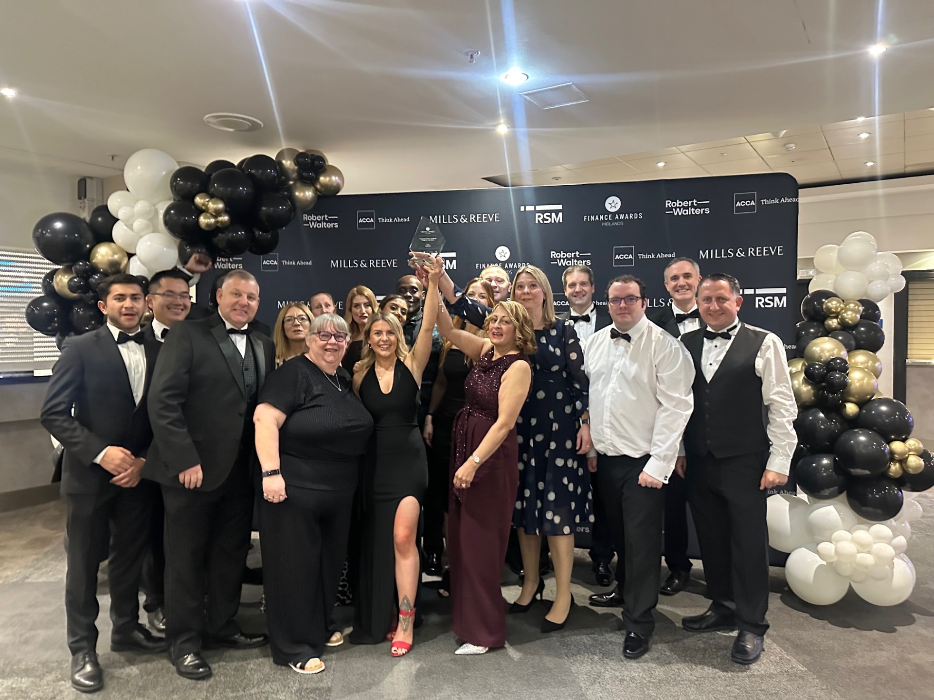 Finance team celebrating award win at West Midlands Finance Awards with trophy and balloon decorations