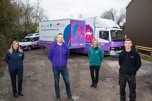 Four individuals in various uniforms stand in front of a service truck branded with 