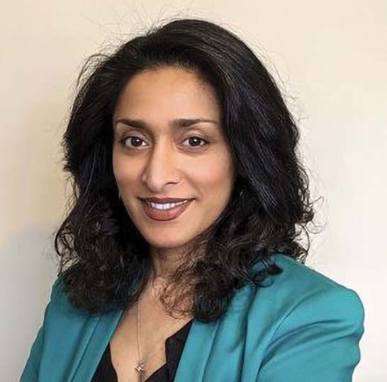 A woman with long, wavy black hair wears a teal blazer over a black shirt, posing against a plain light background.