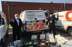 Two men in face masks stand beside a van filled with food donations, promoting community support