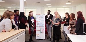 A diverse group of professionals engaged in a collaborative discussion around a presentation board in a modern office setting.