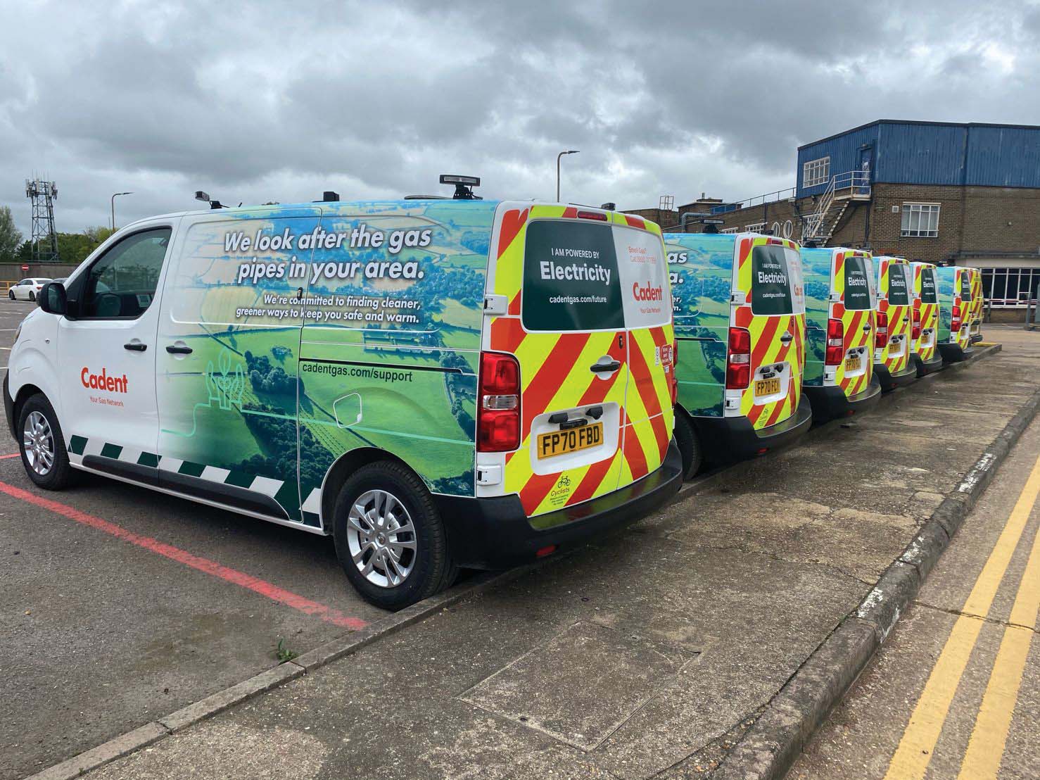 A line of Cadent service vans parked in a lot, showcasing branding focused on gas and electricity services with safety markings.
