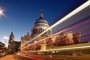 St. Paul's Cathedral illuminated at dusk, with light trails from passing vehicles in the forground