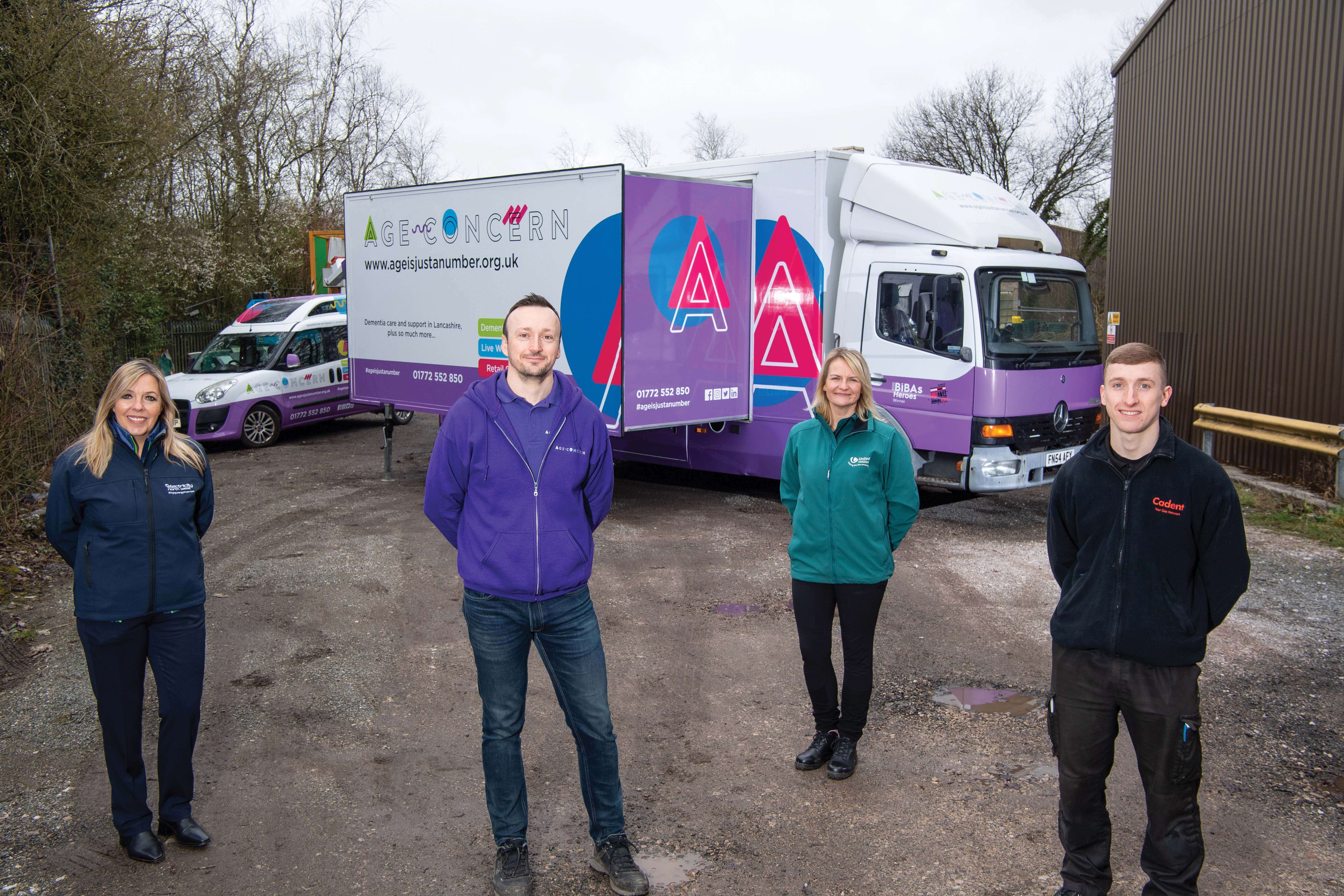 Four individuals in various uniforms stand in front of a service truck branded with 