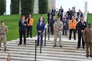 A group of military personnel and civilians stand on steps outdoors, dressed in formal attire, honouring a commemorative event.