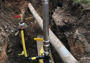 A water pipe installation site showing metallic and yellow pipes in a trench, with valves positioned for control and access.