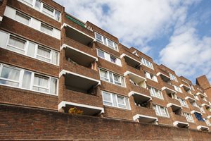 A low-angle view of a brick apartment building with multiple balconies under a partly cloudy sky.
