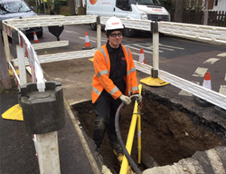 An enginner standing in a hole, surrounded by barriers, repairing a yellow gas pipe following a gas incident in Richmond, North London