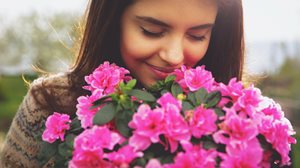 A person holds a vibrant bouquet of pink flowers against a softly blurred natural background