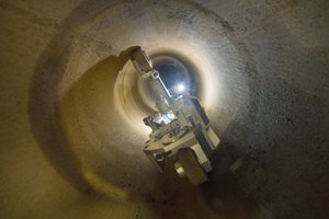 A CISBOT vehicle navigates a dimly lit underground tunnel, illuminated by lights, with smooth, curved walls surrounding it.