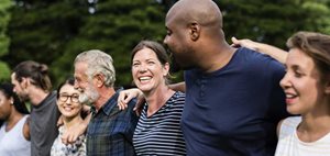 A diverse group of people stands close together outdoors, smiling and displaying a sense of unity in a natural setting.