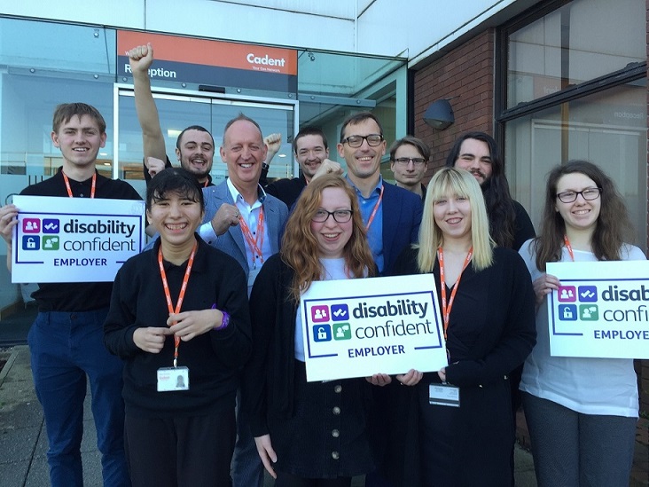 A group of employees stands outside a Cadent office, proudly holding signs that read 