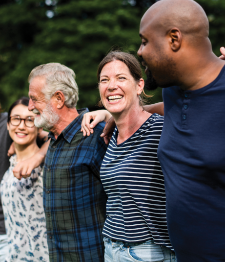 A diverse group of five people stands arm in arm outdoors, sharing smiles and enjoying each other's company in a green park setting.